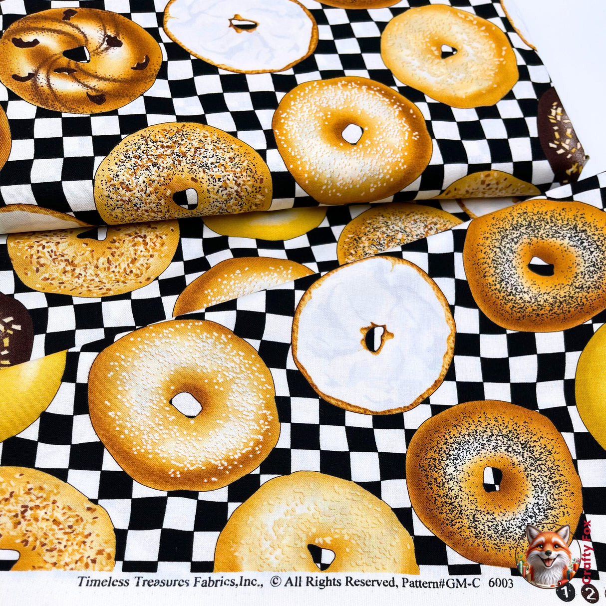 Bagel fabric on fabric bolt, with fabric folded over to show easement of fabric. this shows a variety of various top coated bagels. This is Quilting, Cotton, Novelty Fabric, by Timeless Treasures Fabrics - Fabric Code TT-GM.C6003