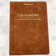 Tan-brown faux suede crossword puzzle book with gold lettering featuring over 130 crossword puzzles