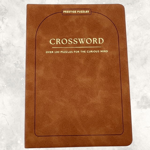 Tan-brown faux suede crossword puzzle book with gold lettering featuring over 130 crossword puzzles