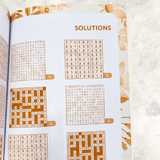 Mixed Puzzle Book opened to the solutions section displaying completed crossword, Sudoku and word search puzzles