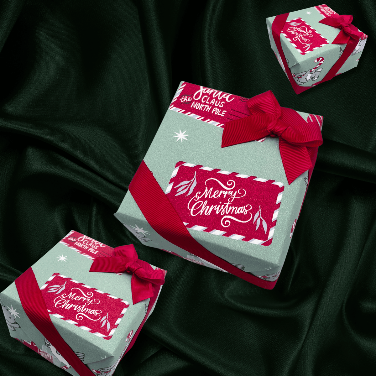 Three wrapped gift boxes with red ribbons and festive labels reading 'Merry Christmas' and 'Santa Claus North Pole' arranged on a dark green satin fabric background.