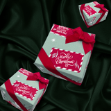 Three wrapped gift boxes with red ribbons and festive labels reading 'Merry Christmas' and 'Santa Claus North Pole' arranged on a dark green satin fabric background.