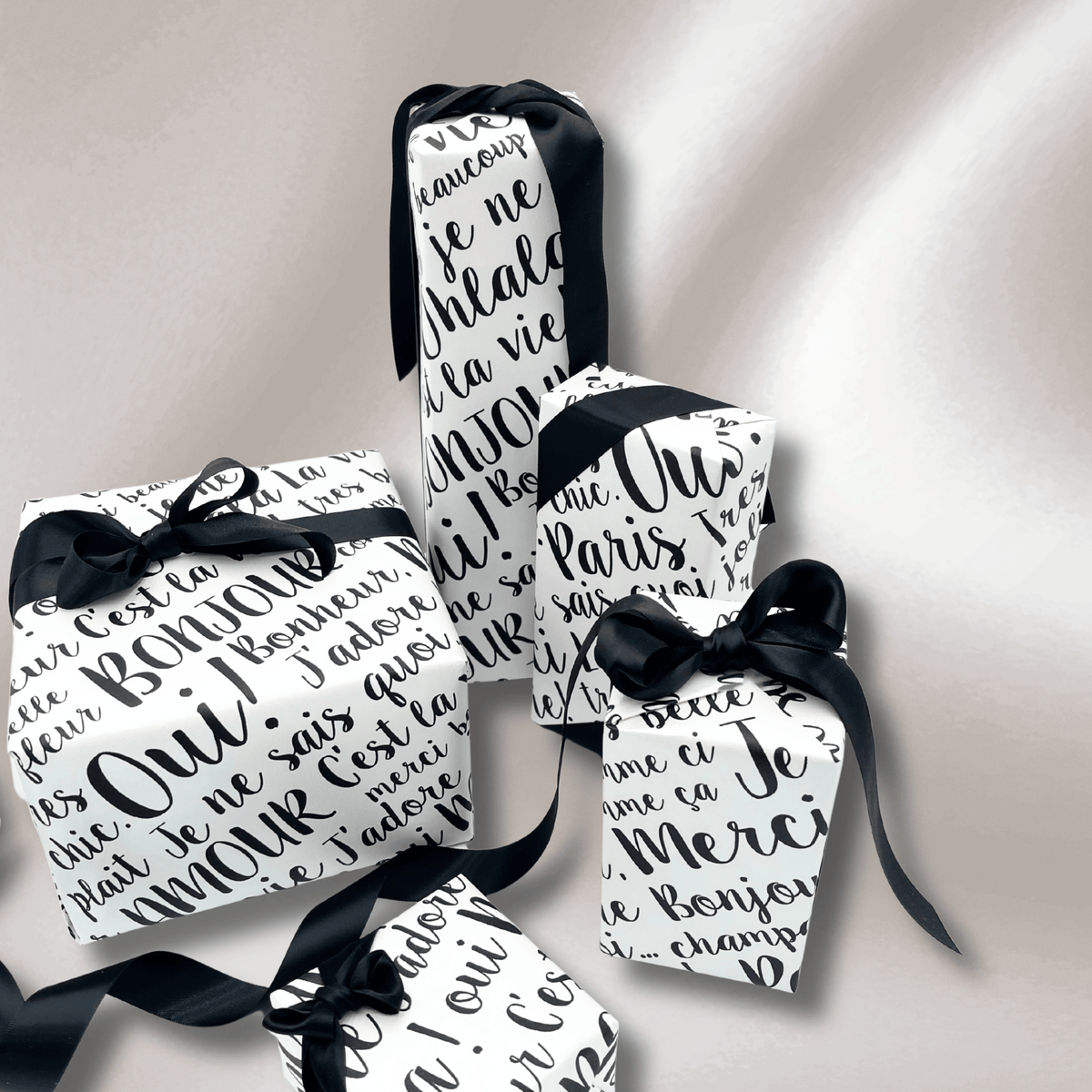 Elegant tall and rectangular gifts wrapped in Paris French typography pearlised paper, styled with black satin ribbon.