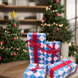 Electric blue and pink checkerboard Christmas wrapping paper on presents decorated with red ribbon beside a festive Christmas tree