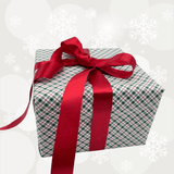 A square gift box wrapped in green and white plaid wrapping paper with a large red ribbon tied in a bow on top, set against a light gray holiday-themed background with white snowflakes.