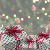 Three wrapped Christmas presents with green and white gingham paper and shiny red ribbons, arranged in front of a softly blurred Christmas tree with warm lights.