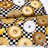 Bagel fabric on fabric bolt, with fabric folded over to show easement of fabric. this shows a variety of various top coated bagels. This is Quilting, Cotton, Novelty Fabric, by Timeless Treasures Fabrics - Fabric Code TT-GM.C6003