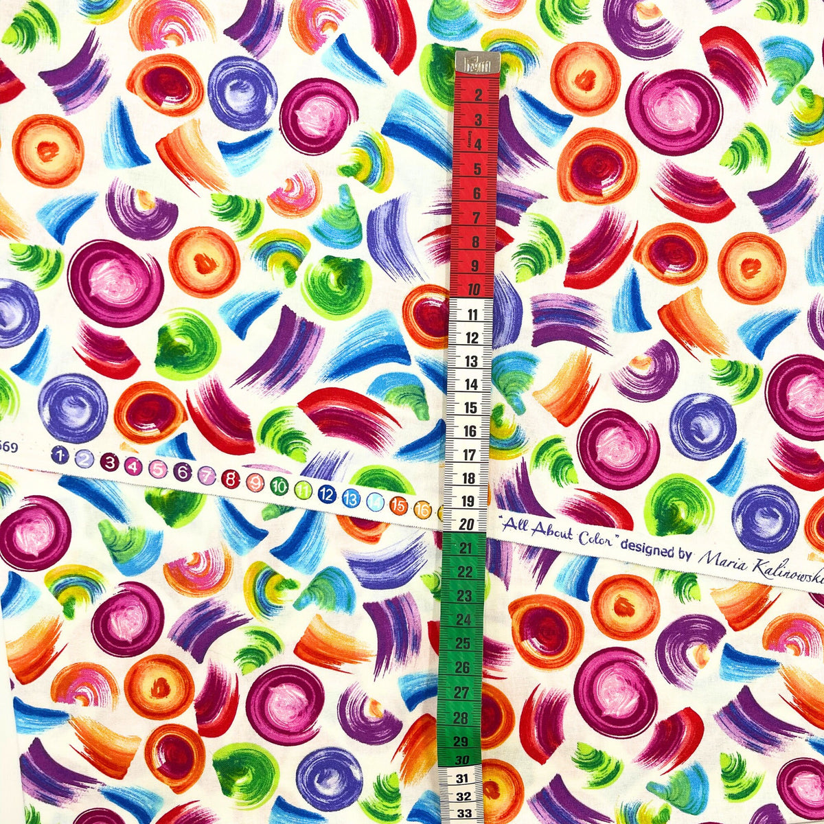 Red, white and green tape measure on selvage of All About Color, multi colour brush strokes on Cream background